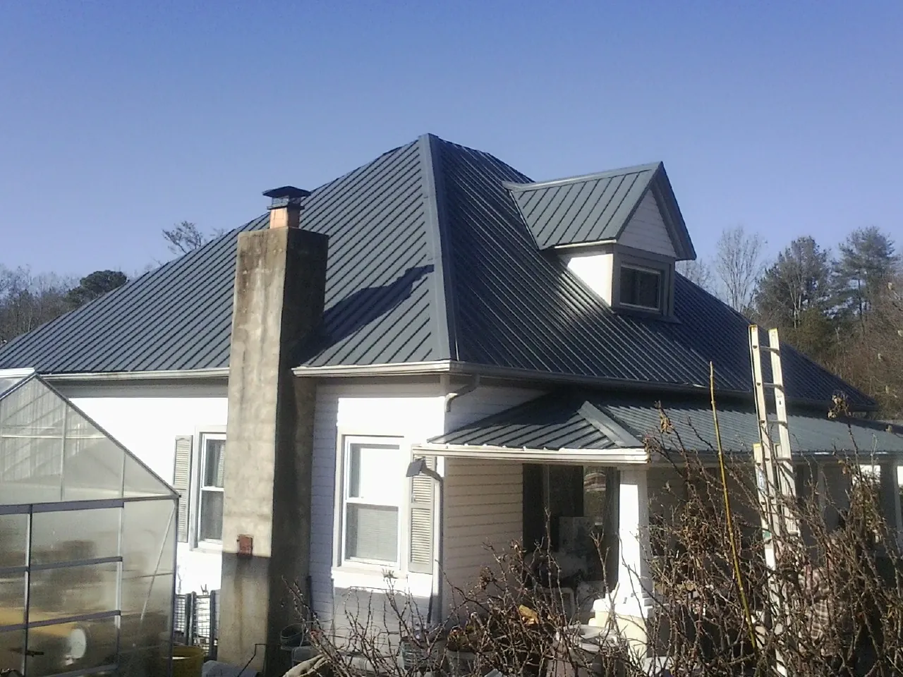 Dark blue standing seam metal roof on a white farmhouse with dormer — Slate & Tile Roof Repair by Roofing Brothers in Methuen
