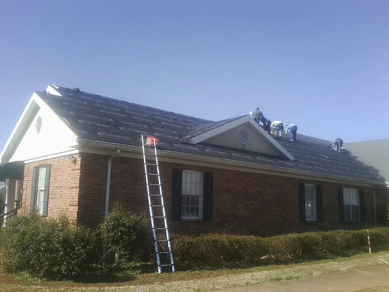 Crew tearing shingles off a brick ranch roof with a ladder set — Metal Roof Repair work by our crew in Methuen