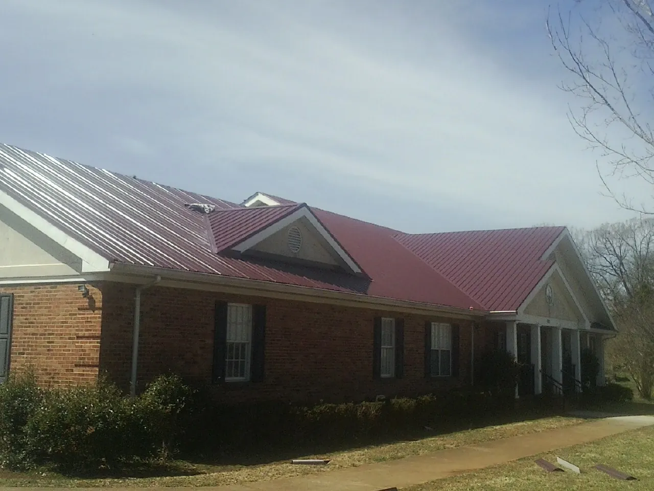 Red metal roof with gabled entries on a long brick building, from a Hail Damage Roof Repair job in Methuen
