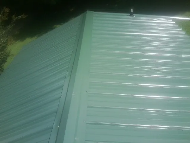 New green metal panels meeting at the ridge of a roof — Flat Roof Repair work by our crew in Methuen
