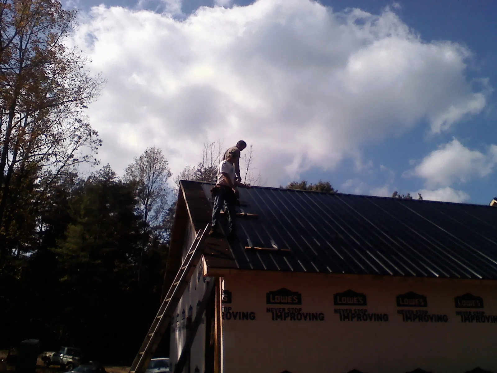 Roofer fastening dark metal panels high against a cloudy sky, from a Roof Inspection job in Methuen