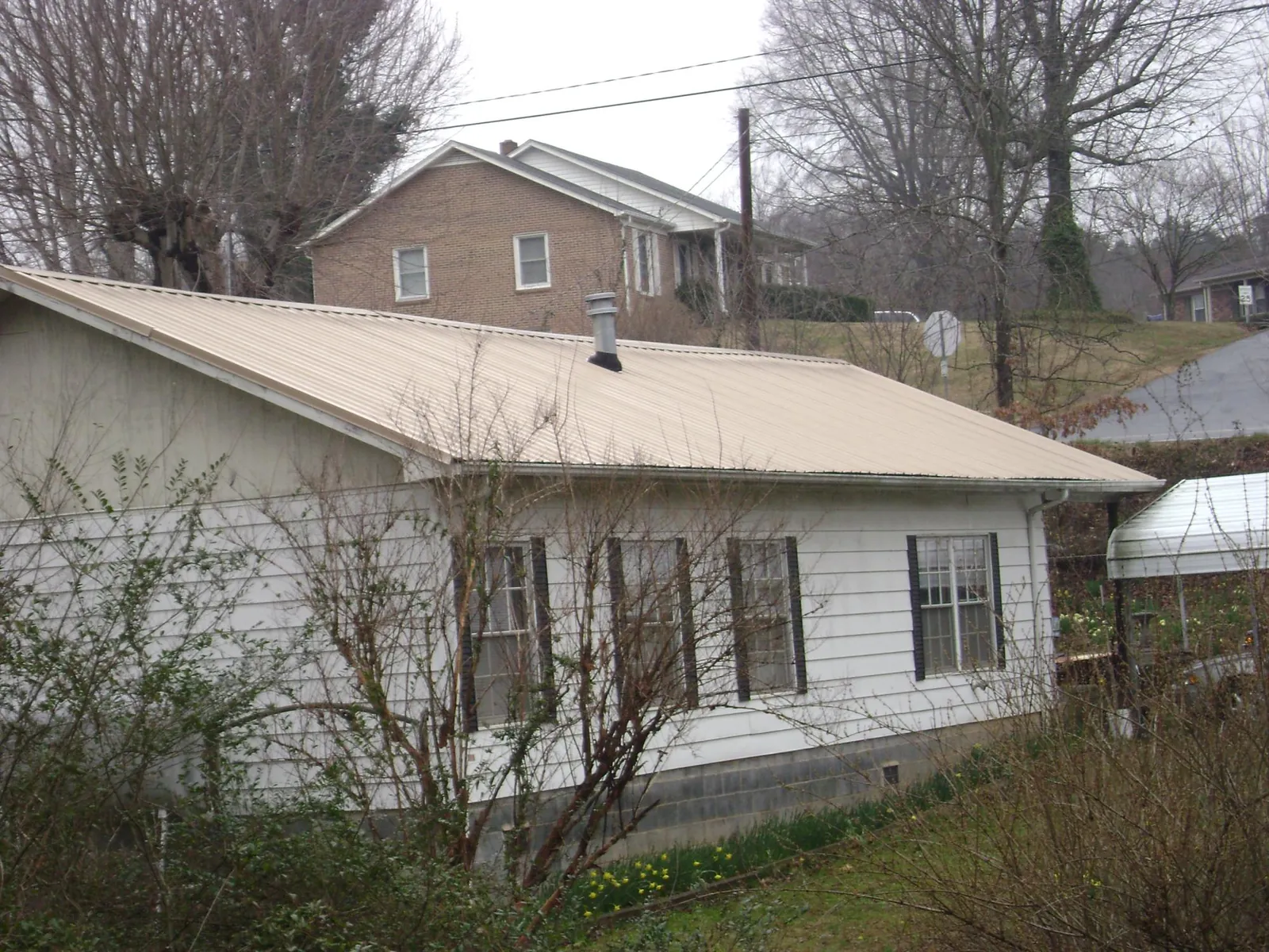 Tan metal roof on a white sided house set into a hillside — Commercial Roofing by Roofing Brothers in Methuen
